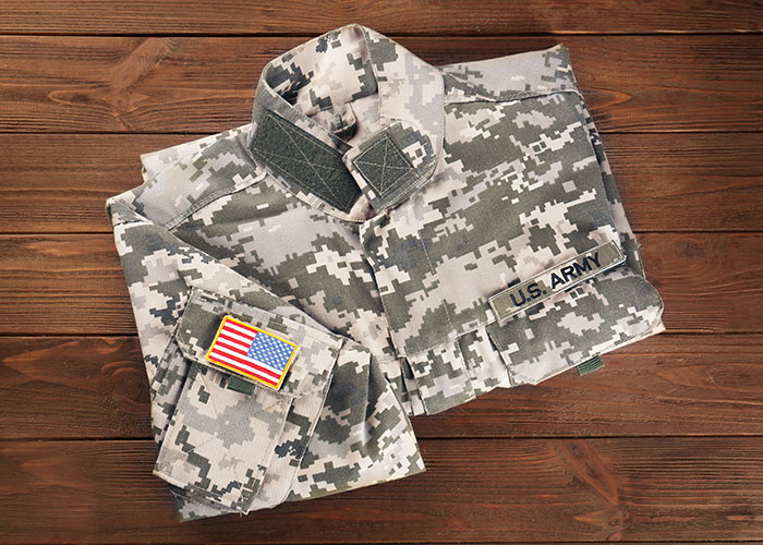 Folded U.S. Army camo jacket with an American flag patch on wooden background, highlighting military attire.