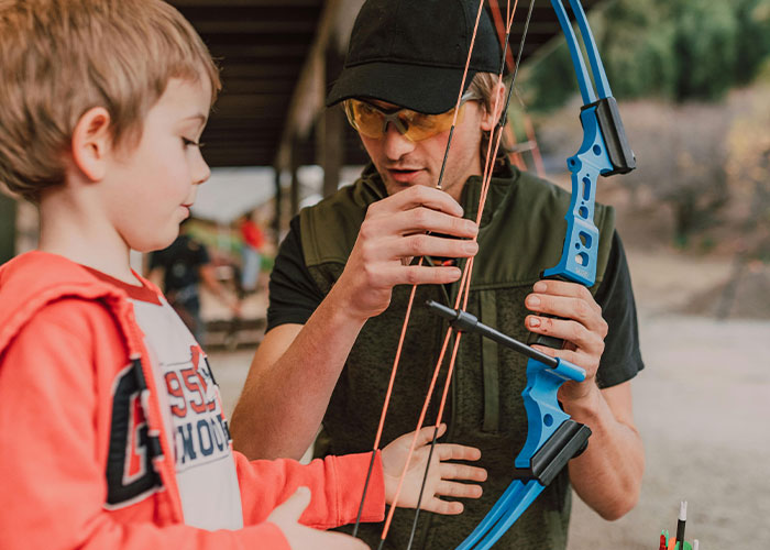 Man teaching child archery, both focused on a blue bow, illustrating a common mistake despite guidance.