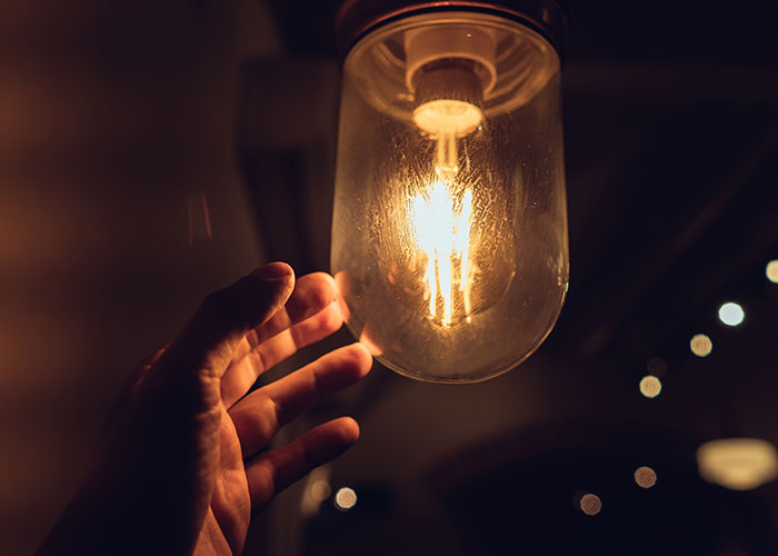 Hand touching a glowing light bulb indoors.