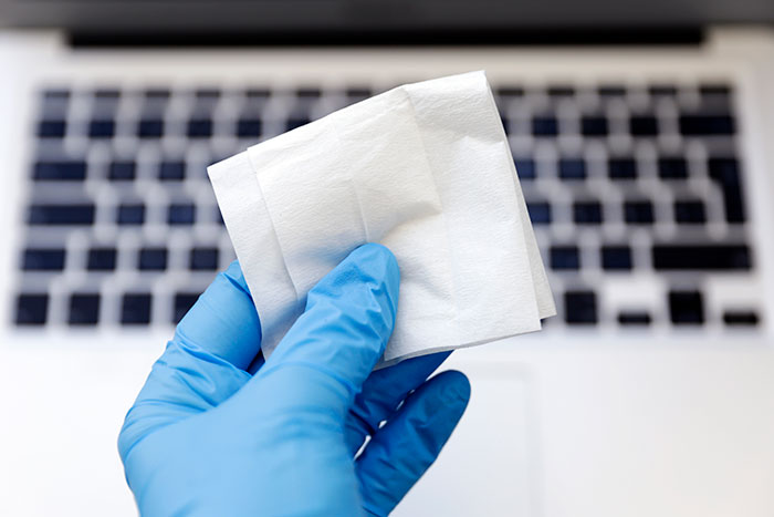 Gloved hand holding wipes over a laptop keyboard, illustrating lifesaving cleaning hacks.