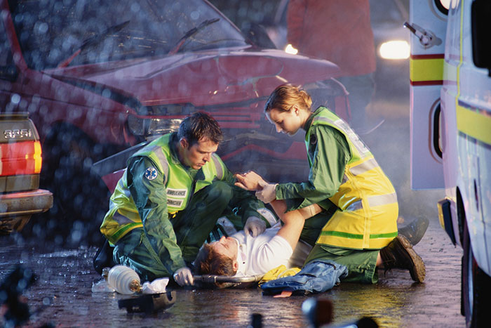 Paramedics attending to a person on the ground near a car accident, highlighting lifesaving actions.