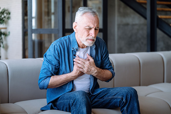 Elderly man clutching chest, sitting on a sofa, illustrating lifesaving warning signs.
