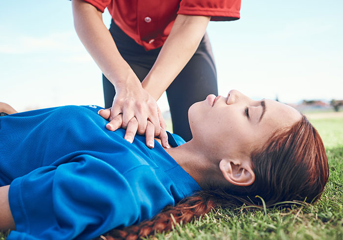 Person performing CPR on woman in a sports field, illustrating lifesaving techniques.