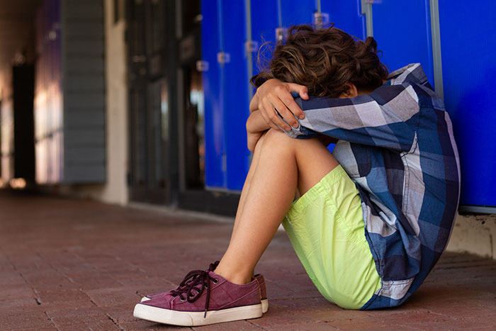 Child sitting alone by lockers, head down, in a checkered shirt; insightful lifesaver moments for well-being.