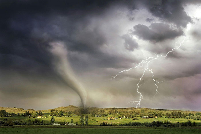 Tornado and lightning striking a green landscape under dark storm clouds, depicting a powerful and surprising natural event.