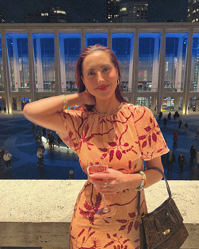Woman in floral dress holding a drink, posing at a nighttime city event; related to plastic surgery discussion.