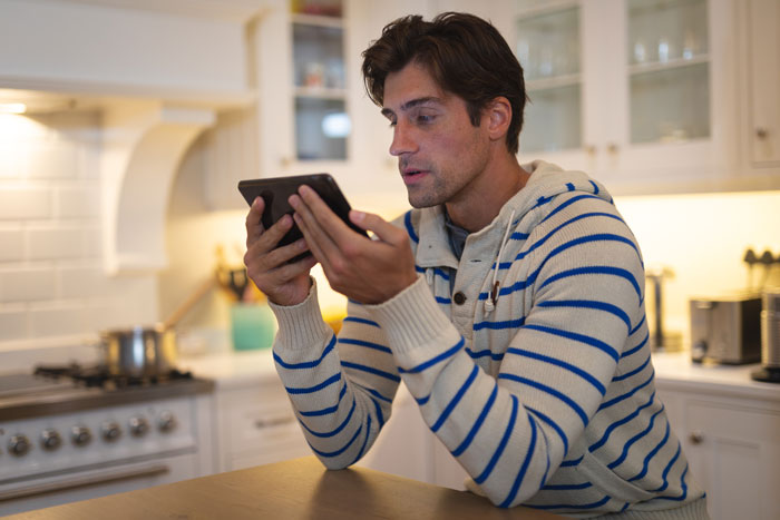 Man in kitchen using tablet, wearing striped sweater, related to engagement pic post issue on Instagram.