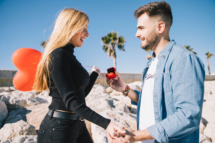 Woman holds heart balloon while man presents engagement ring, symbolizing a joyful proposal moment.