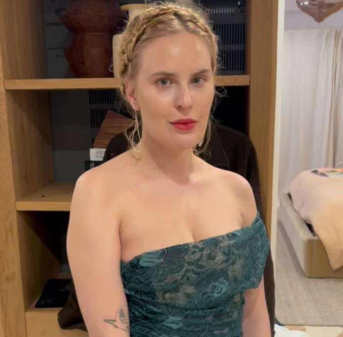 Demi Moore's daughter in a teal dress, standing in a room with a bookshelf and bed in the background.