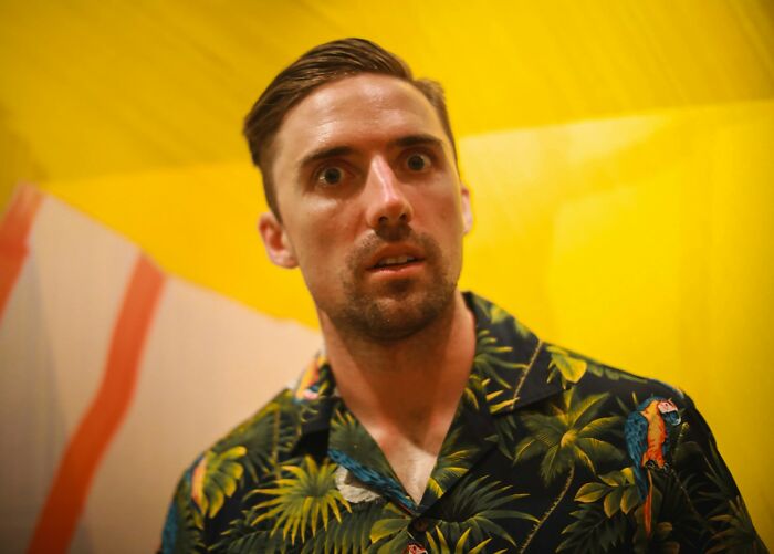Man in a tropical shirt looks surprised, standing against a yellow background, illustrating the importance of trusting your gut.