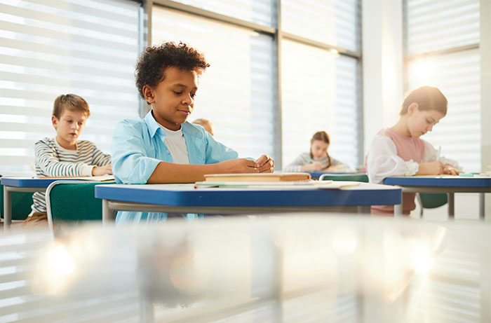 Students concentrating on their work in a classroom setting, with sunlight filtering through the windows.