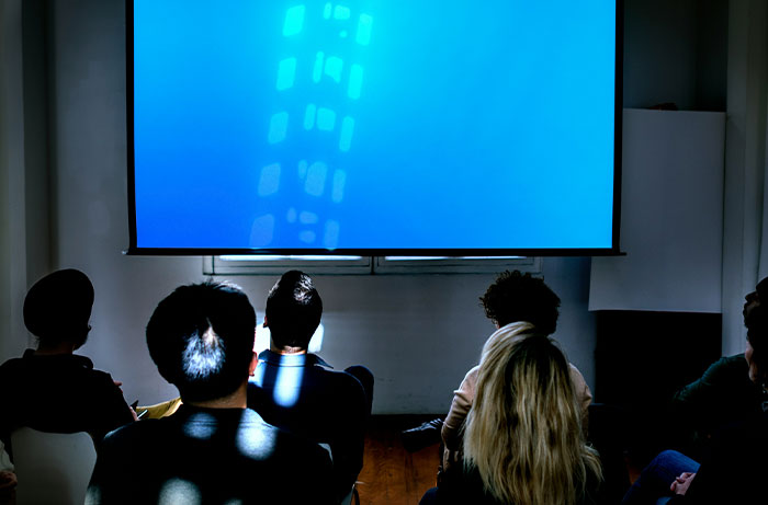 Students sitting in a classroom watching a bright blue projection screen, symbolizing the teacher's hidden insights.
