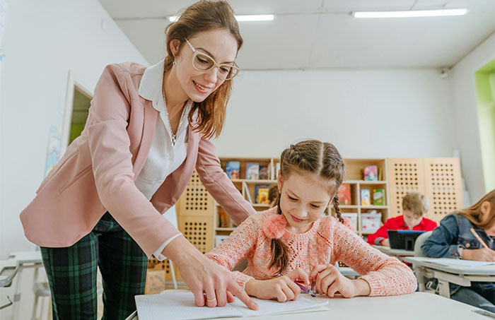 Teacher helping a student in the classroom, engaging in educational activities and maintaining authority.