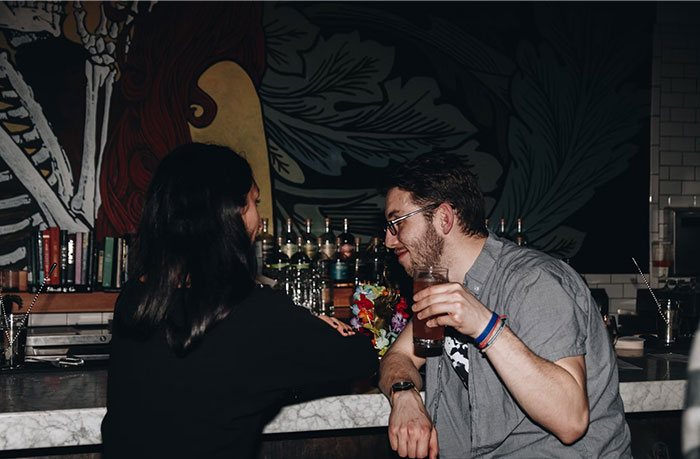 A man and woman chatting at a bar, surrounded by eclectic decor, highlighting a casual setting.