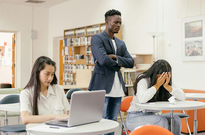 Teacher supervising students in a library, one stressed, highlighting authority.