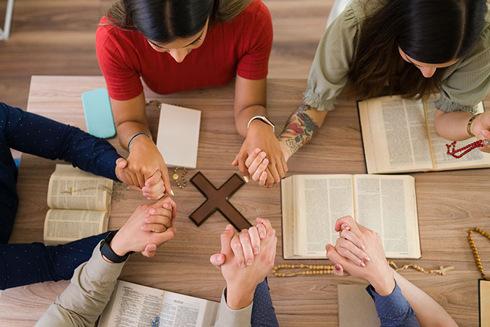 Group of people holding hands and praying over open Bibles with wooden cross, reflecting family drama and refusal to babysit.