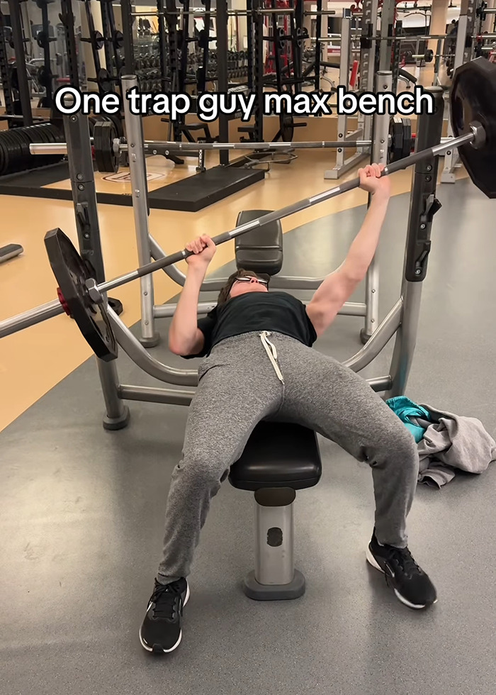 A young man bench pressing in a gym, displaying uneven muscle development by working out only one side of his body.