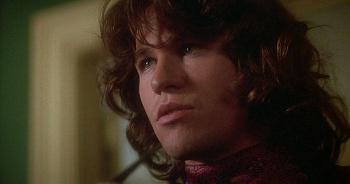 Actor in costume with curly hair and patterned scarf, portraying a difficult role with intense expression for a film scene.