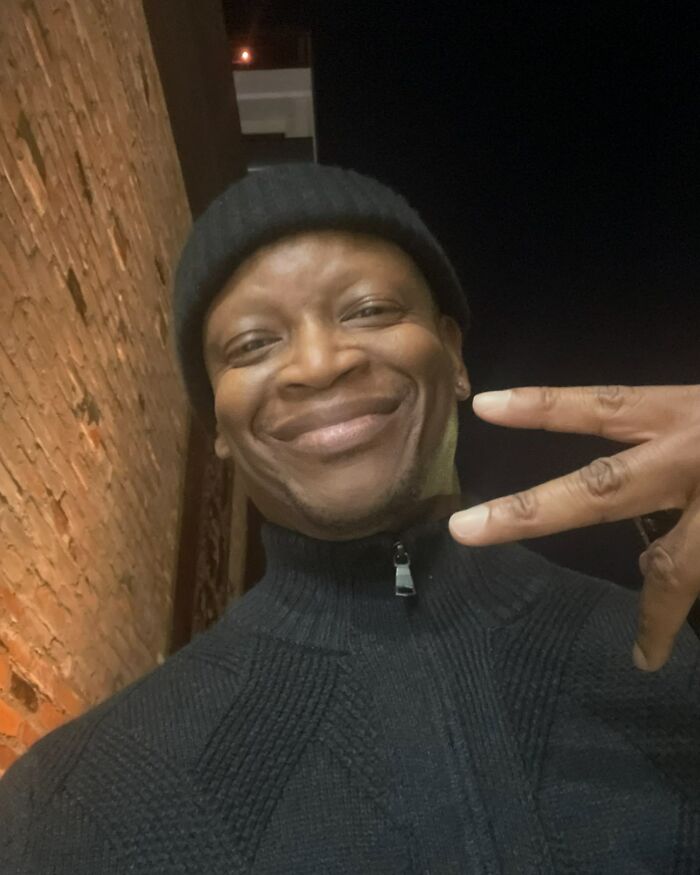 Man smiling warmly, wearing a beanie, making a peace sign, showcasing celebrity kindness in real life.