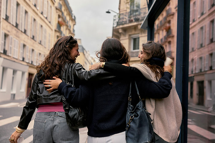 Three friends walking arm in arm down a European street, symbolizing unique cultural aspects of Europe.