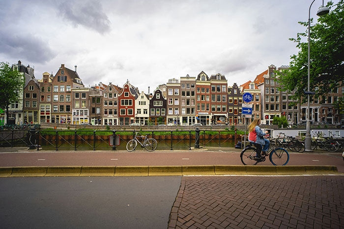 Cyclist rides along a canal in Europe, passing charming row houses under a cloudy sky.