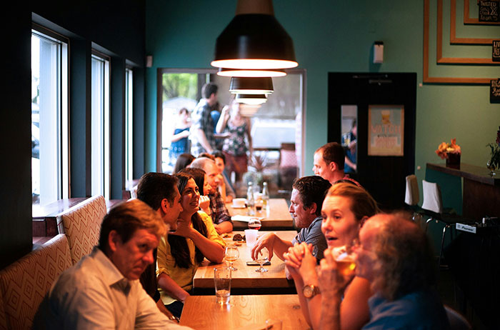 People dining in a European cafe, chatting and enjoying drinks at a long table.