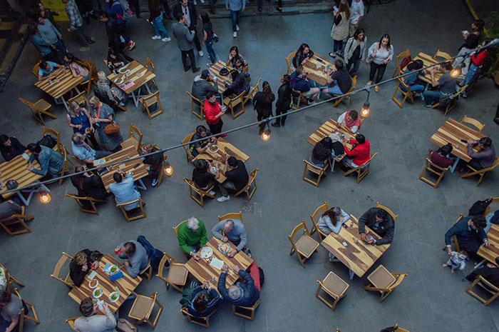 Aerial view of a bustling European cafe with many people sitting at wooden tables.