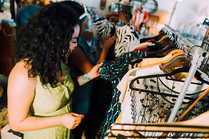 Women shopping for clothes at a thrift store, finding creative ways to save money during economic challenges.