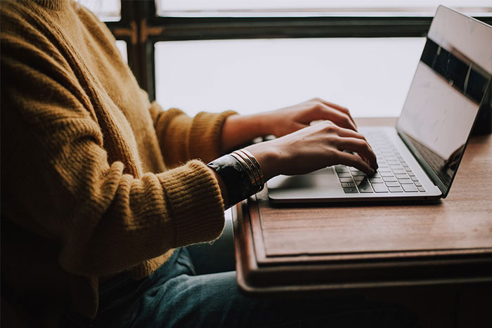 Person in a yellow sweater typing on a laptop, symbolizing money saving during economic challenges.