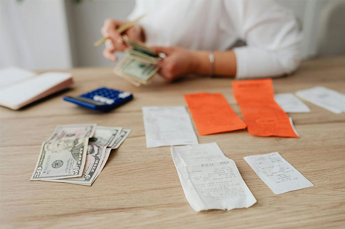 Person managing money and receipts on a table, illustrating money-saving tips from the Great Recession.