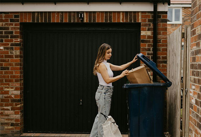 Woman practicing money saving, reusing items from recycling bin outside a brick garage.
