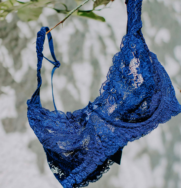 Blue lace bra hanging outside against a wall, with leafy branches in the background, unrelated to motorcycle helmet topic.