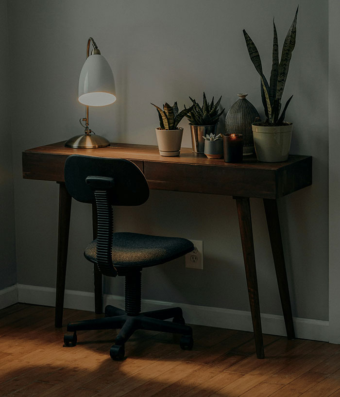 A dimly lit wooden desk with potted plants and a lamp, beside an office chair, no motorcycle helmet present.