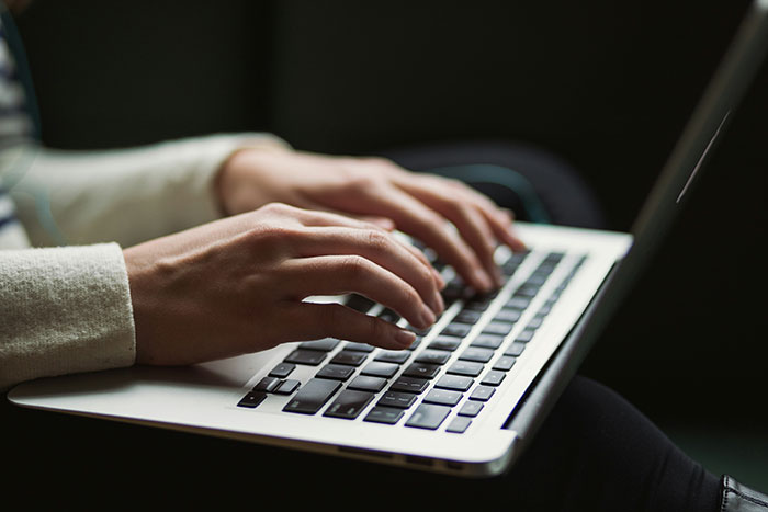 Hands typing on a laptop keyboard, focused on digital content creation.