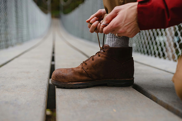 Person tying laces on brown boots while crossing a suspension bridge, focusing on outdoor footwear instead of motorcycle helmet.
