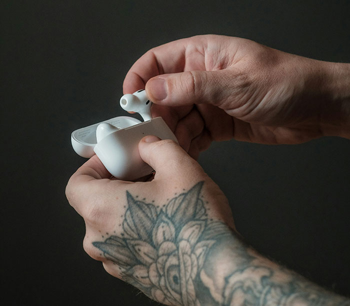 Hands with tattoos holding earbuds, showcasing care in handling electronics.