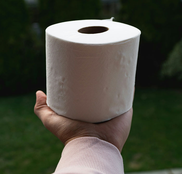 Hand holding a roll of toilet paper outdoors, unrelated to motorcycle helmet topics.
