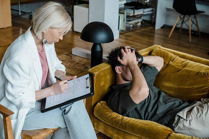 Therapist taking notes while a man sits on a couch, reflecting on a life-changing decision for safety.