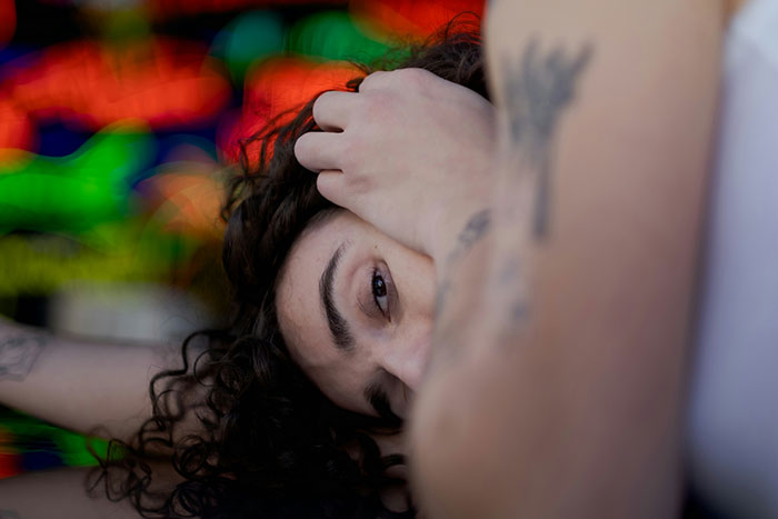 Person with tattoos resting head, colorful abstract background, reflecting on life-changing safety decisions.