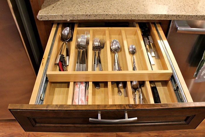 Open kitchen drawer with organized cutlery, highlighting areas to clean before hosting guests.
