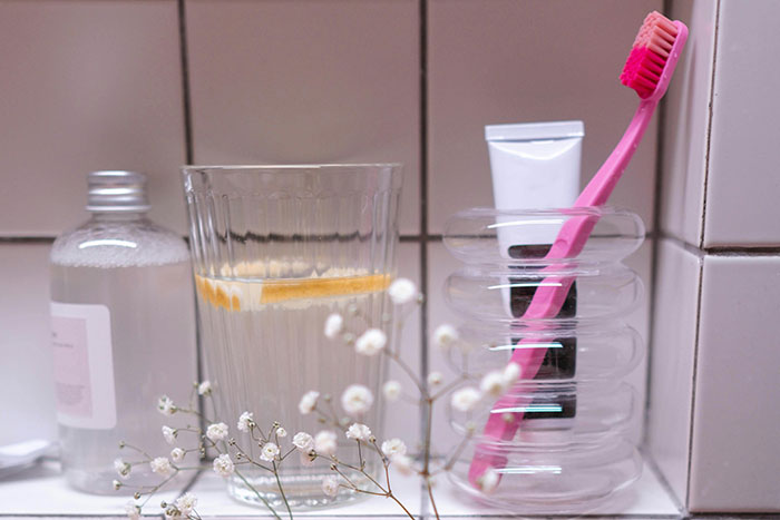 Toothbrush and toothpaste beside a glass with a slice of lemon, highlighting items people shouldn't forget to clean before guests.