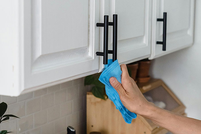 Cleaning cabinet handles with a blue cloth, highlighting home cleaning tips before hosting guests.