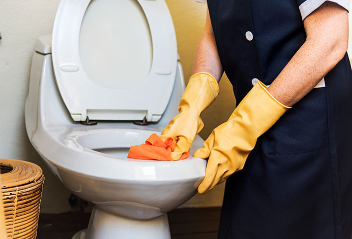 Person wearing gloves cleaning a toilet, emphasizing essential cleaning before hosting guests.