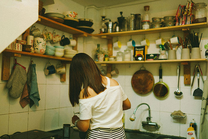 Woman in kitchen surrounded by shelves of dishes, cooking in a familiar and nostalgic environment.