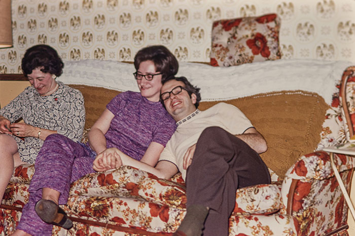 Three people sitting on a floral sofa in a vintage living room, capturing a once normal moment in the past.