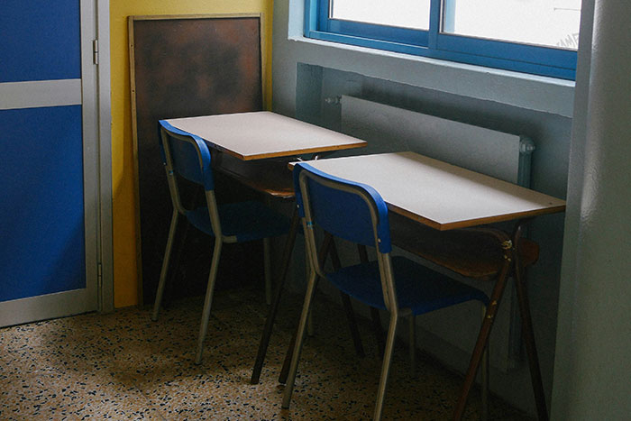 Two empty classroom desks and chairs near a window, reminiscent of how normal schools once were.