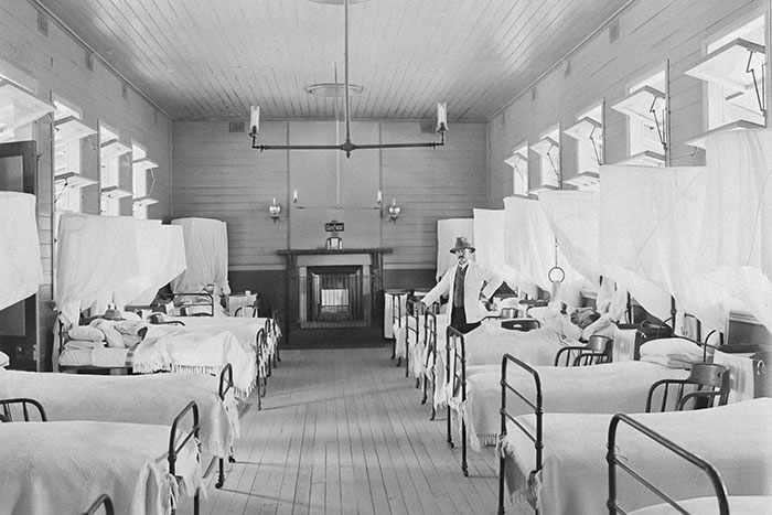 Historic hospital ward with patients in beds, showcasing early 20th-century healthcare practices, a reminder of past normals.