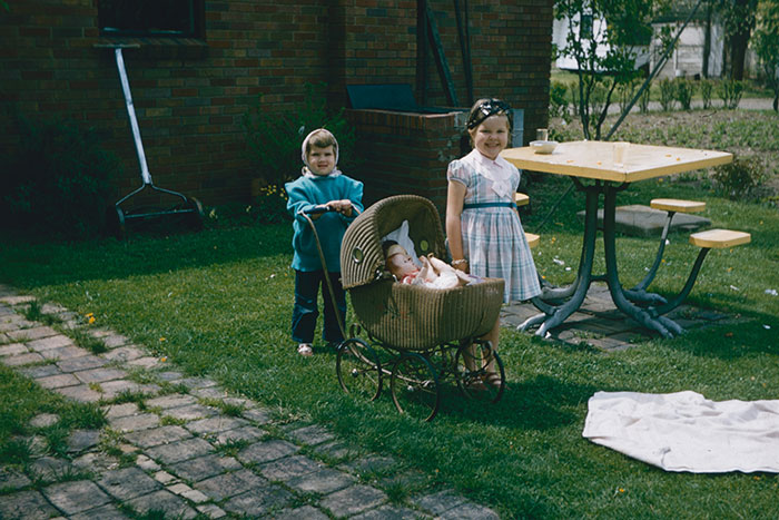 Children in vintage attire with a pram in a backyard, showcasing things that might shock people in 2025.
