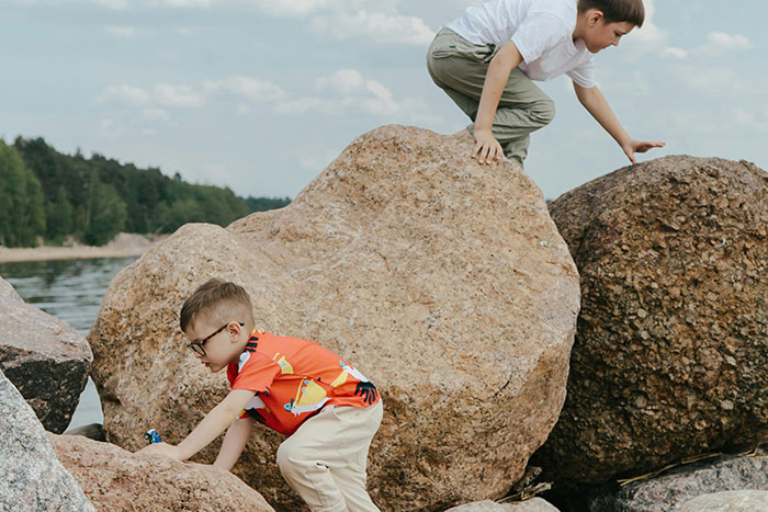 Children playing on large rocks by the water, a scene recalling normal past activities.
