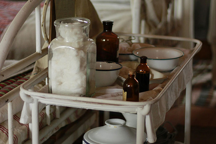 Vintage medical supplies on a hospital cart, including glass jars and bowls, evoke nostalgia of a once-normal past.